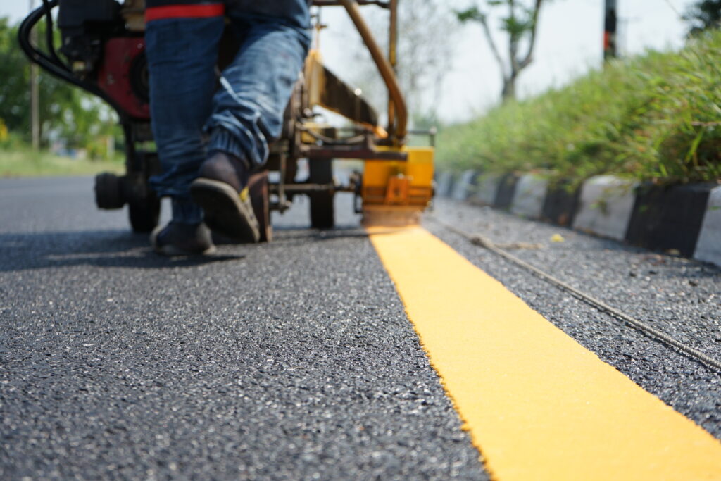 Yellow traffic line being painted by a worker with a machine on fresh asphalt pavement
