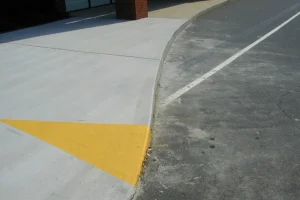 Concrete sidewalk ramp with yellow detectable warning panel next to an asphalt roadway.