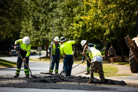multiple paving contractors working with tools to spread fresh asphalt paving