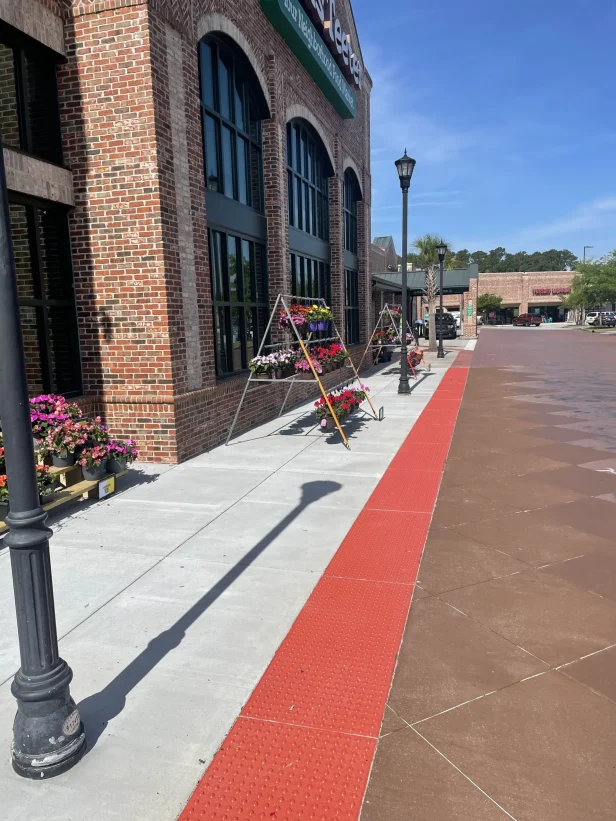 Concrete walkway in front of a store with tactile curbing. There are two displays with various flowers on the sidewalk.