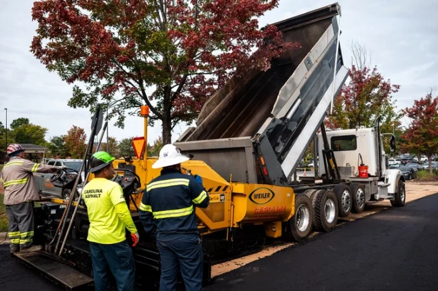 asphalt milling and paving truck dumping asphalt milling on top of roadway while paving contractors lay it down using another machine