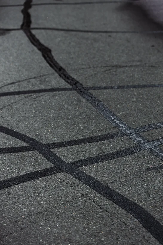 Asphalt crack sealing with black filler applied to damaged pavement cracks.