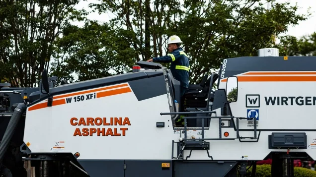 man in safety gear riding on a paving truck with the carolina asphalt logo on it